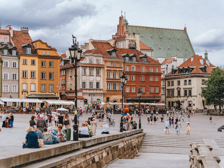 Vibrant summer scene of Warsaw's Old Town Square with people enjoying the historical charm and colorful architecture.