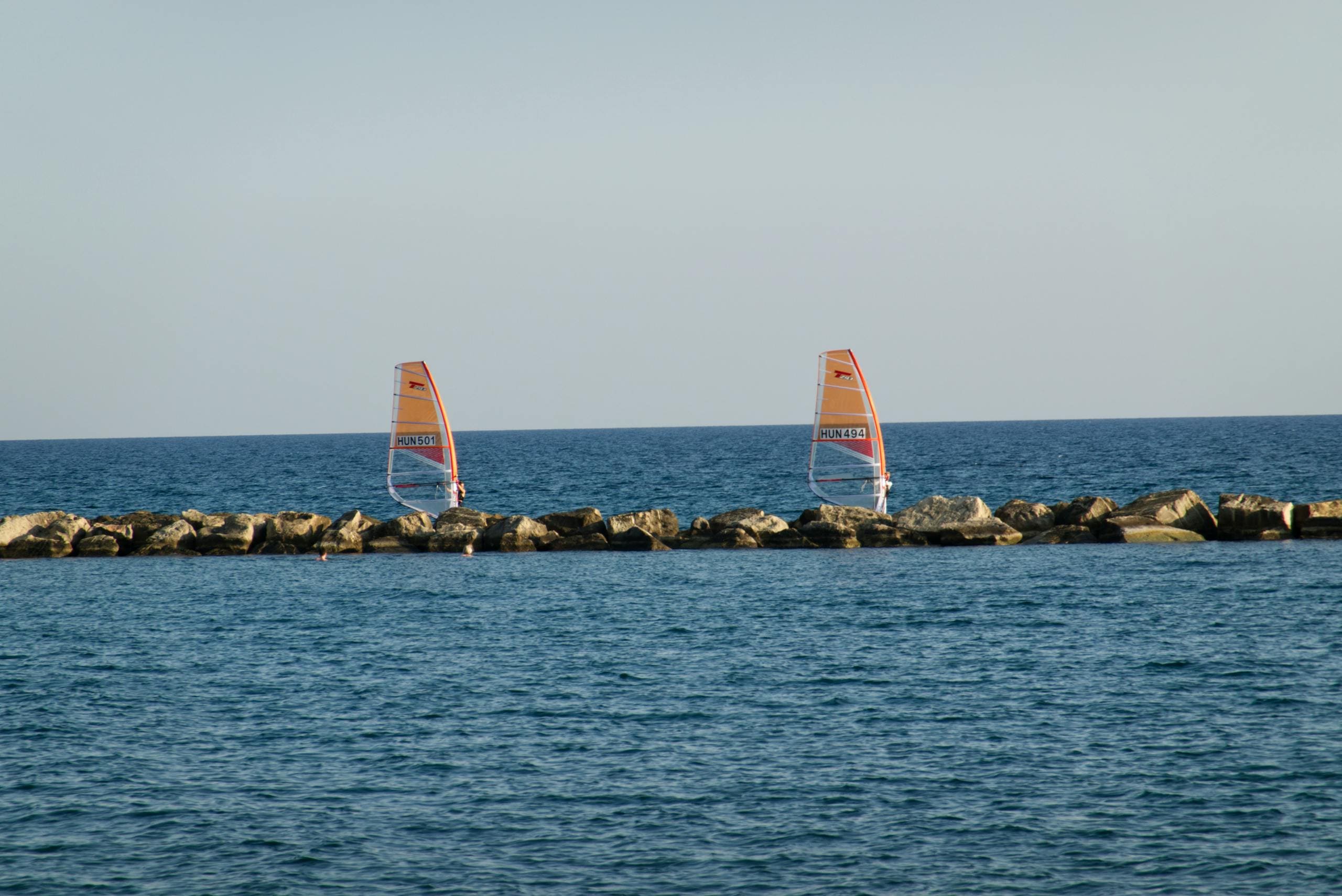 Dwie deski windsurfingowe z pomarańczowymi żaglami na błękitnym morze przy falochronie w Limassol na Cyprze