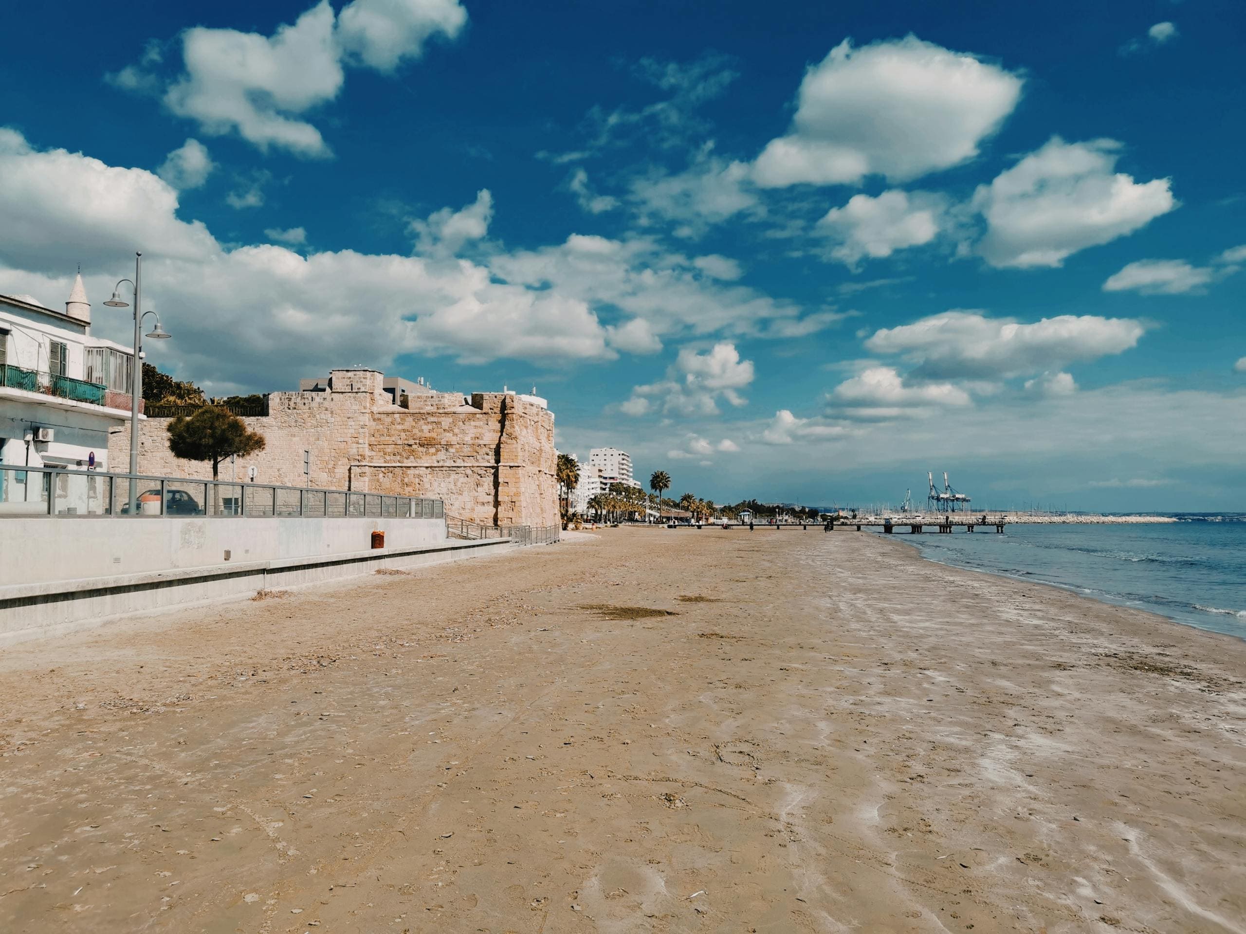 Malownicza plaża ze złotym piaskiem w Larnace na Cyprze z zabytkowym fortem i błękitnym niebem