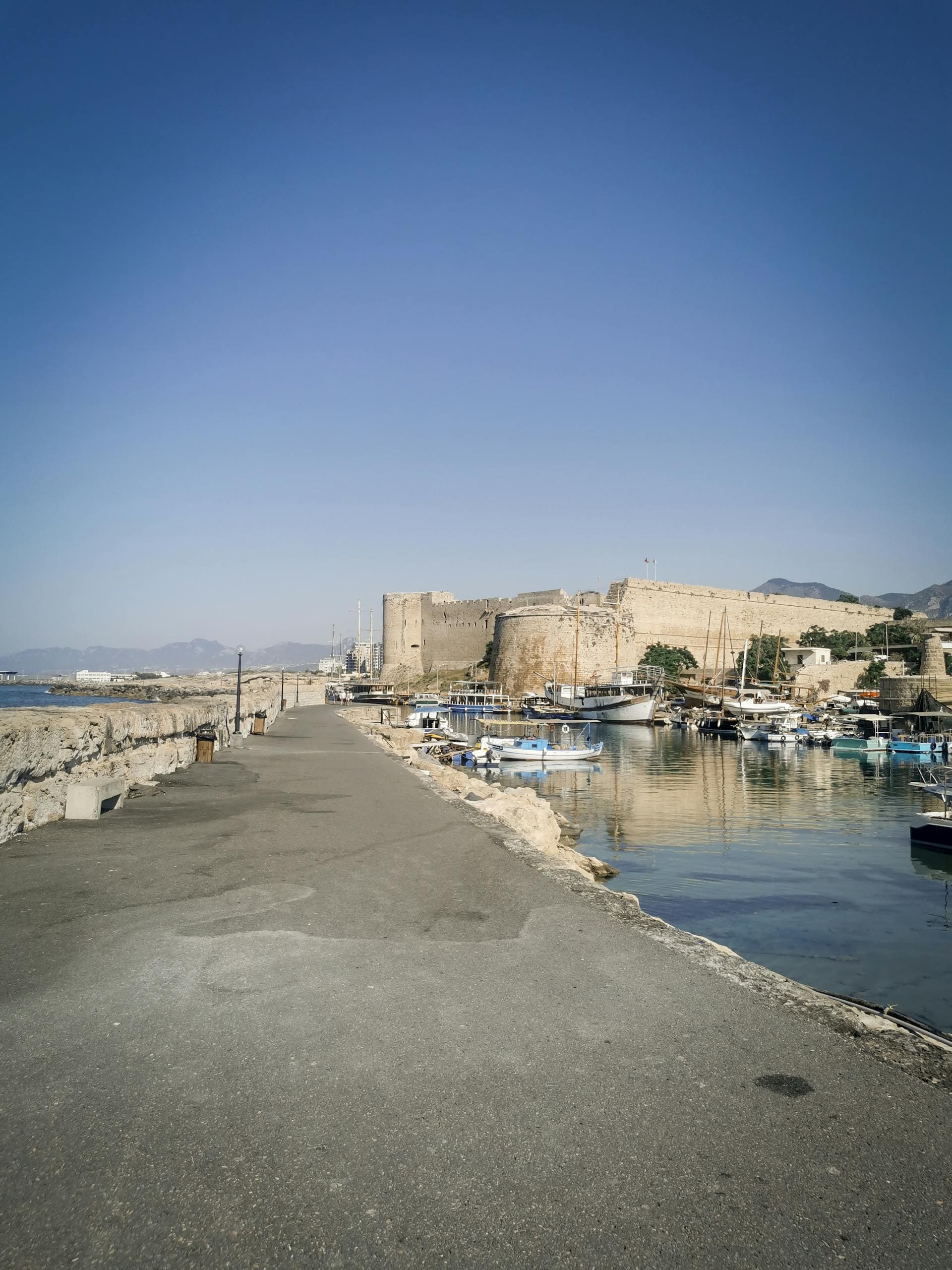 Malowniczy port w Kyrenii na Cyprze z zabytkowym zamkiem i luksusowymi jachtami pod jasnym niebem