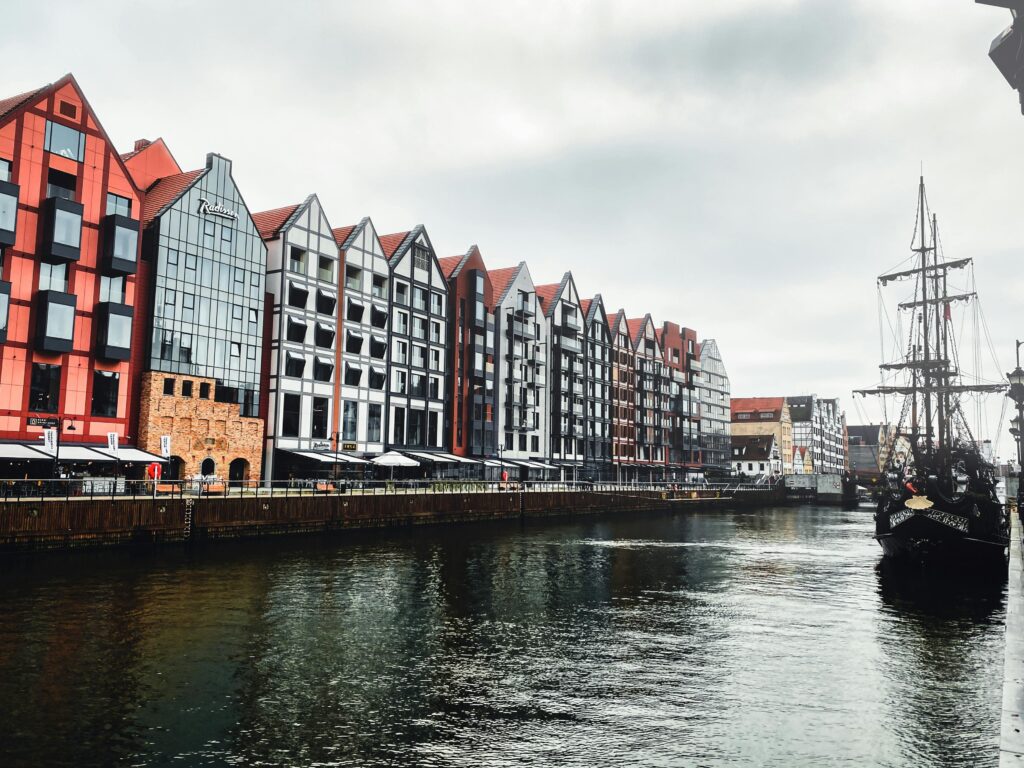Malowniczy widok na Gdańsk z charakterystycznymi kolorowymi kamienicami nad rzeką Motławą i zabytkowym żaglowcem. Urokliwa panorama nadrzecznego bulwaru w historycznym centrum miasta.