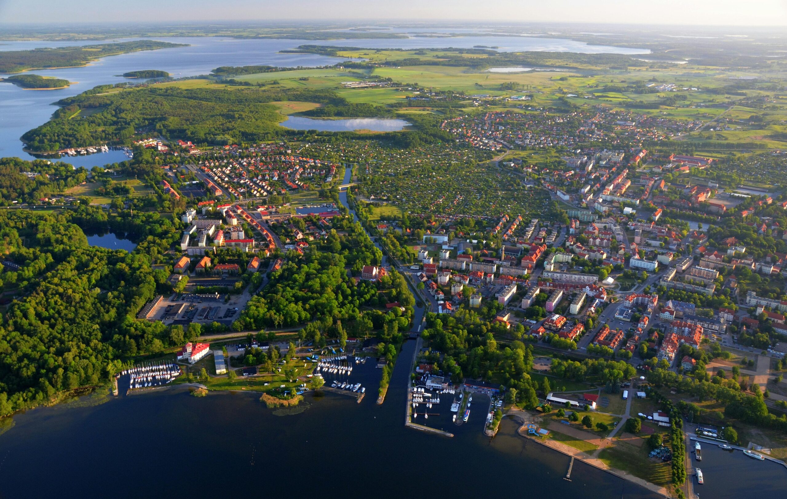 Spektakularny widok z lotu ptaka na mazurskie miasto nad jeziorem z mariną jachtową i zielenią. Kraina Tysiąca Jezior - idealne miejsce na żeglarstwo, wypoczynek i turystykę wodną w Polsce.