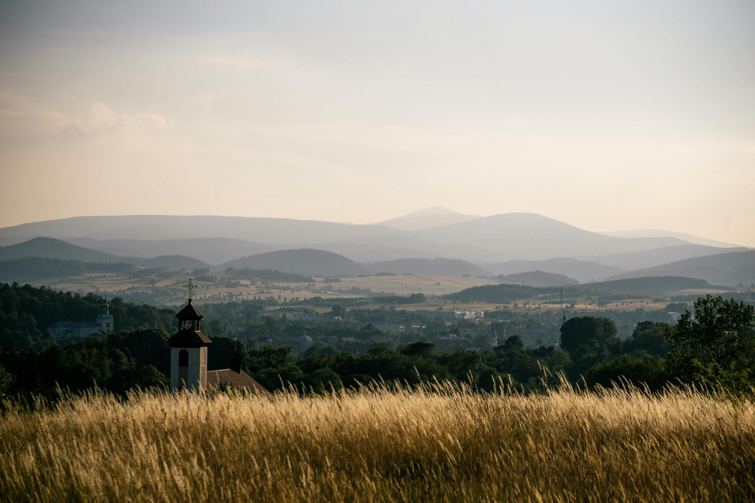 Malowniczy widok na małą kapliczkę w krajobrazie Sudetów z panoramą gór i złotymi łąkami. Tradycyjna architektura religijna w polskich górach - spokojny krajobraz na tle pasma górskiego.