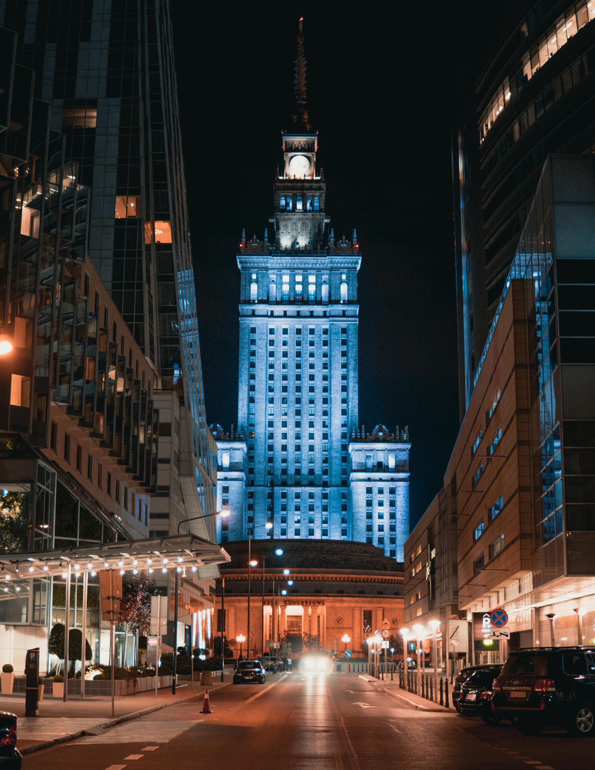 Spektakularny nocny widok na Pałac Kultury i Nauki w Warszawie z podświetleniem. PKiN otoczony nowoczesnymi wieżowcami centrum stolicy - magiczna atmosfera warszawskich ulic po zmroku.