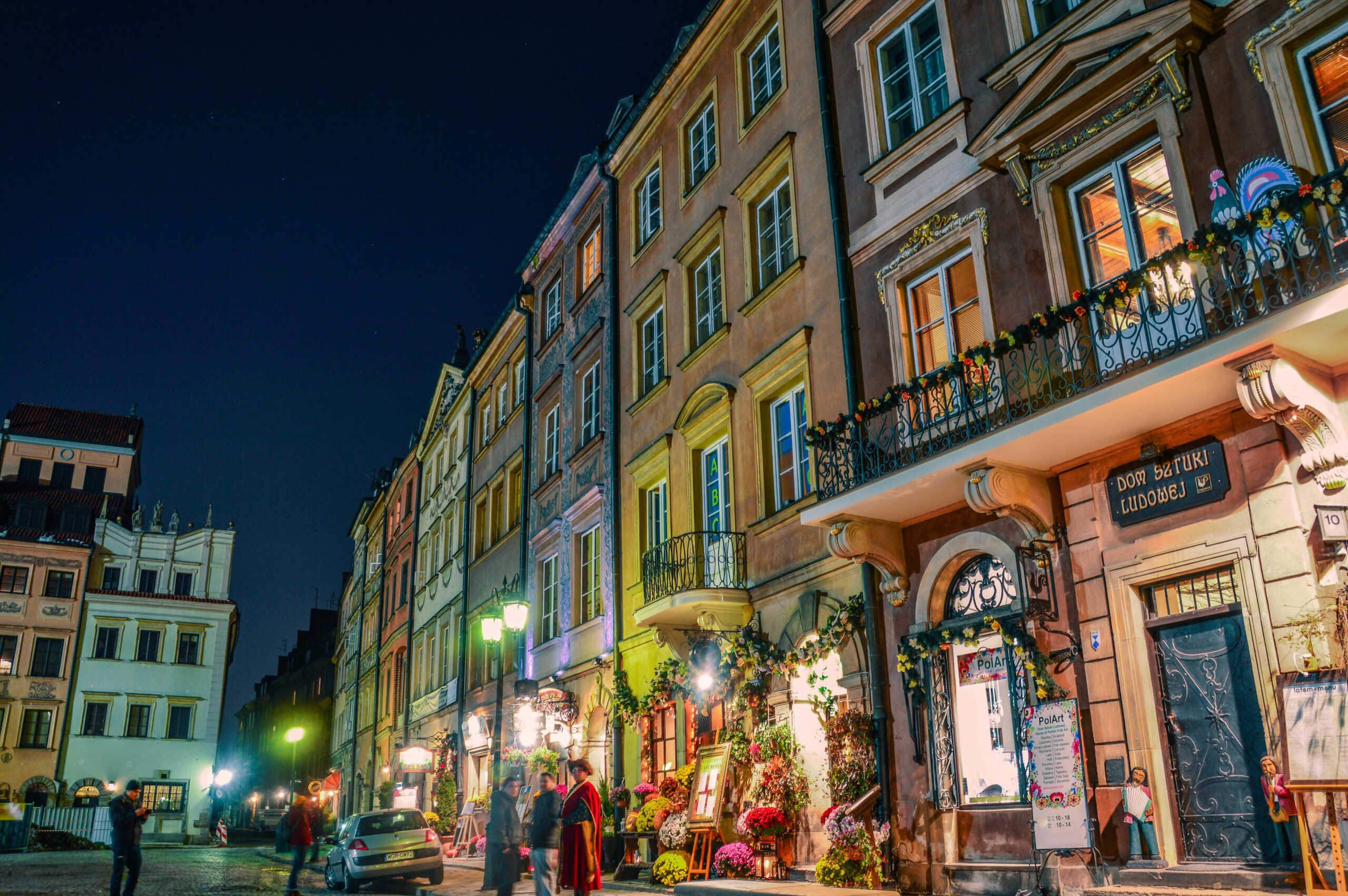 Magiczny nocny widok na kolorowe kamieniczki Starego Miasta w Warszawie z restauracjami i kawiarniami. Klimatyczne oświetlenie zabytkowych budynków UNESCO - romantyczna atmosfera wieczornej Warszawy.