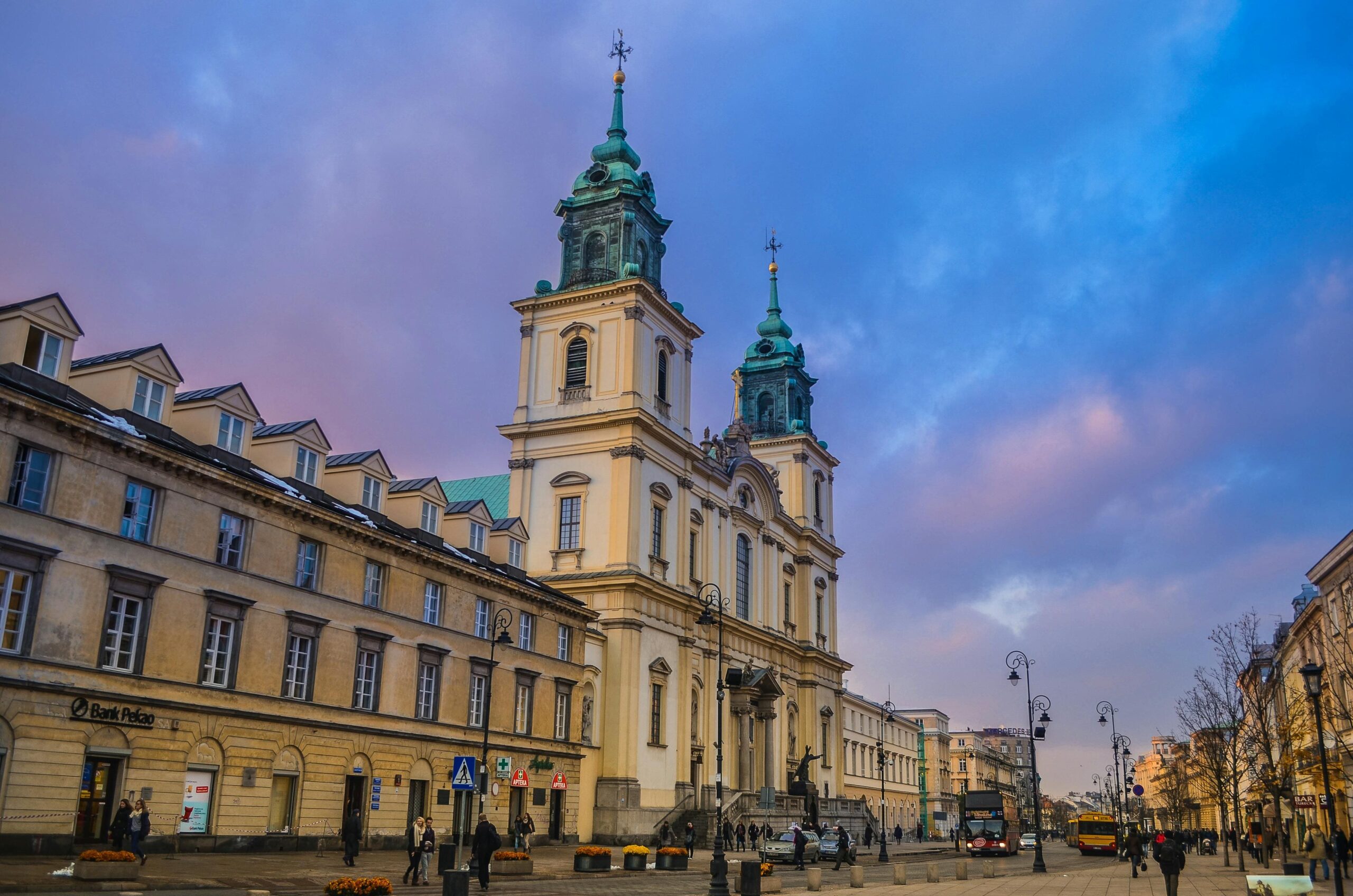 Barokowy Kościół Świętego Krzyża na Krakowskim Przedmieściu w Warszawie w wieczornym oświetleniu. Zabytkowa architektura religijna w centrum stolicy z charakterystycznymi zielonymi kopułami.