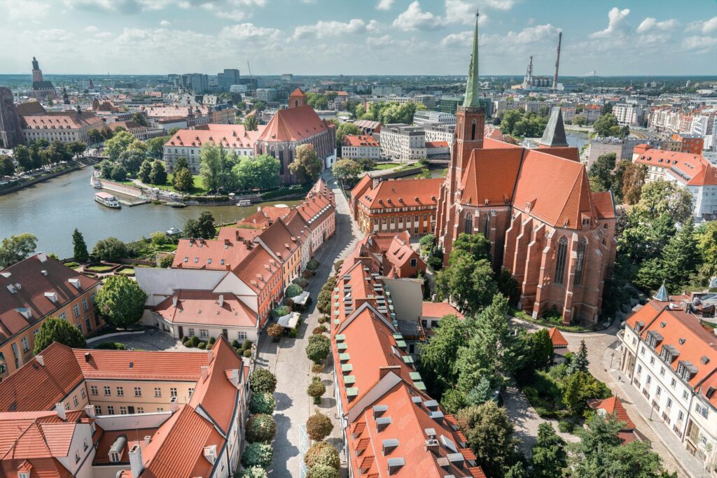 Spektakularny widok z drona na Wrocław z charakterystycznymi czerwonymi dachówkami, imponującą gotycką katedrą i rzeką przepływającą przez miasto. Unikalna panorama zabytkowego centrum Wrocławia z wysokości ptaka.