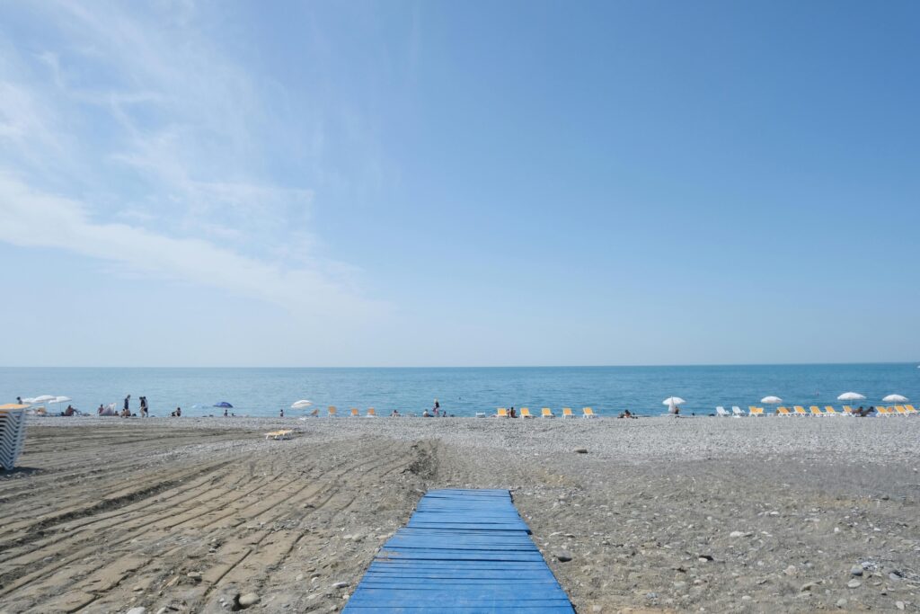 Letnia plaża w Batumi w Gruzji z drewnianym niebieskim pomostem, kolorowymi parasolami plażowymi i leżakami rozstawionymi wzdłuż brzegu Morza Czarnego pod jasnym niebem z chmurami