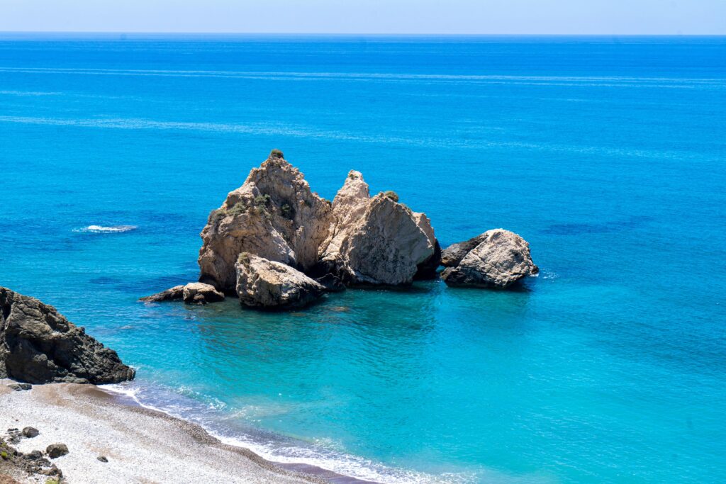 Słynna skała Afrodyty (Petra tou Romiou) na Cyprze z turkusową wodą Morza Śródziemnego i białą piaszczystą plażą. Legendarne miejsce narodzin Afrodyty na Cyprze, najważniejsza atrakcja turystyczna wyspy z charakterystycznymi wapiennymi skałami wystającymi z błękitnej wody. Cypryjska plaża przy skale Afrodyty, must-see podczas wakacji na Cyprze, idealne miejsce na zdjęcia i zwiedzanie mitologicznych miejsc na południowym wybrzeżu Cypru.
