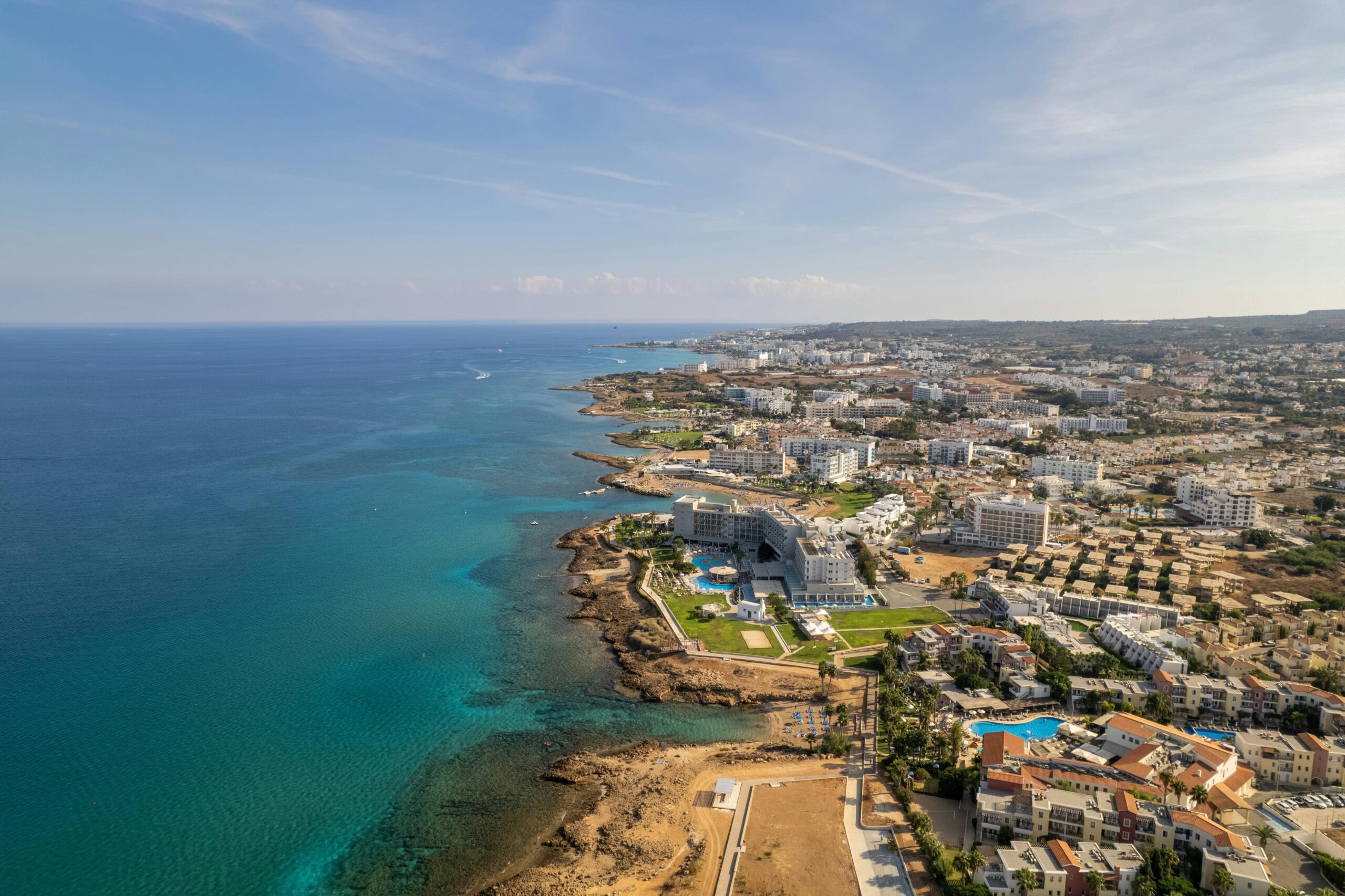 Protaras Cypr z lotu ptaka - panorama hoteli i resortów wzdłuż turkusowego wybrzeża Morza Śródziemnego, wschodnia część Cypru z plażami i skalistymi zatoczkami.