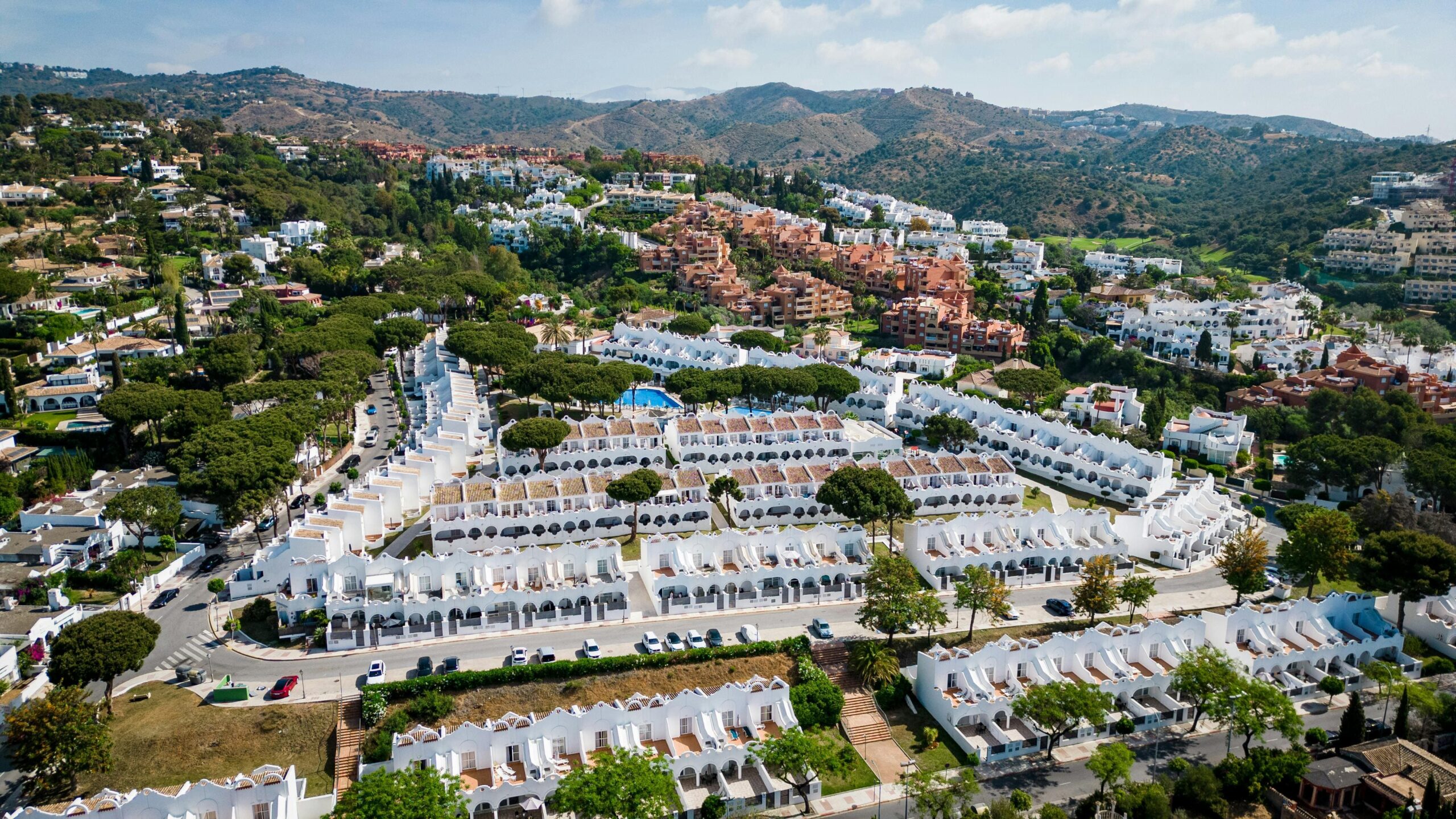 Hiszpania nieruchomości z drona Costa del Sol - białe apartamenty z pomarańczowymi dachami w kompleksie mieszkaniowym, nowoczesne osiedle z basenem w górach Andaluzji, inwestycje mieszkaniowe Hiszpania