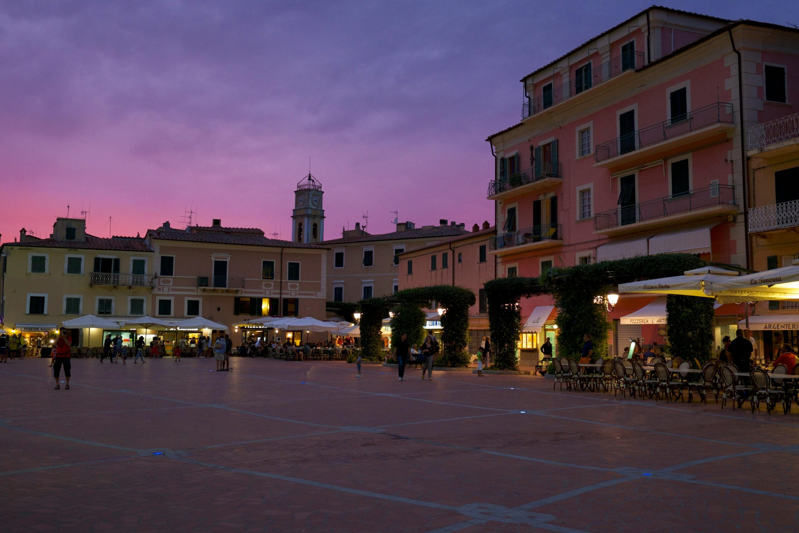Cinque Terre kolorowe domy o zmierzchu - włoskie miasteczko z wieżą zegarową na piazza, kawiarnie i restauracje na głównym placu, fioletowe niebo nad Ligurią o zachodzie słońca