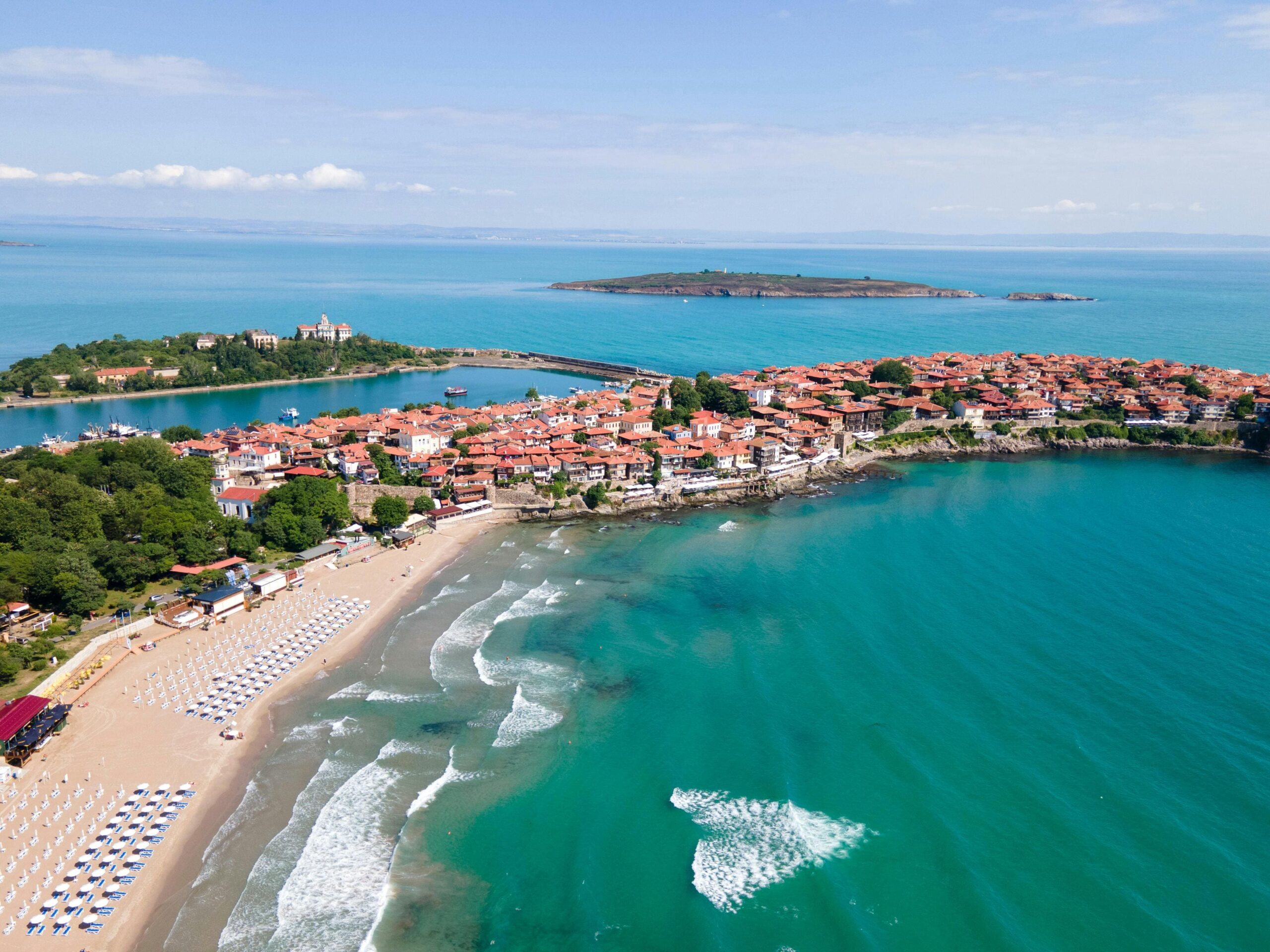 Bułgaria Sozopol zatoka z turkusową wodą z drona - historyczne miasteczko z czerwonymi dachami na półwyspie, piaszczysta plaża z parasole i krystaliczne morze, ekskluzywne nieruchomości nad Morzem Czarnym członkostwo UE