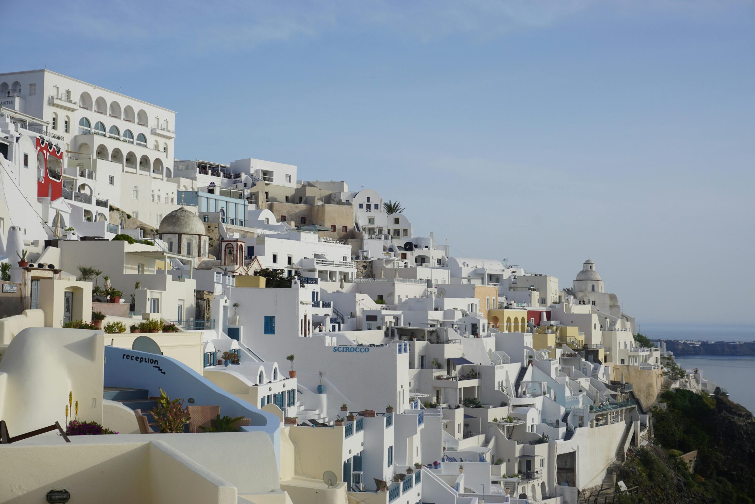 Gęsta biała zabudowa hoteli i apartamentów w Firze na Santorini schodzących tarasami po klifie, Grecja