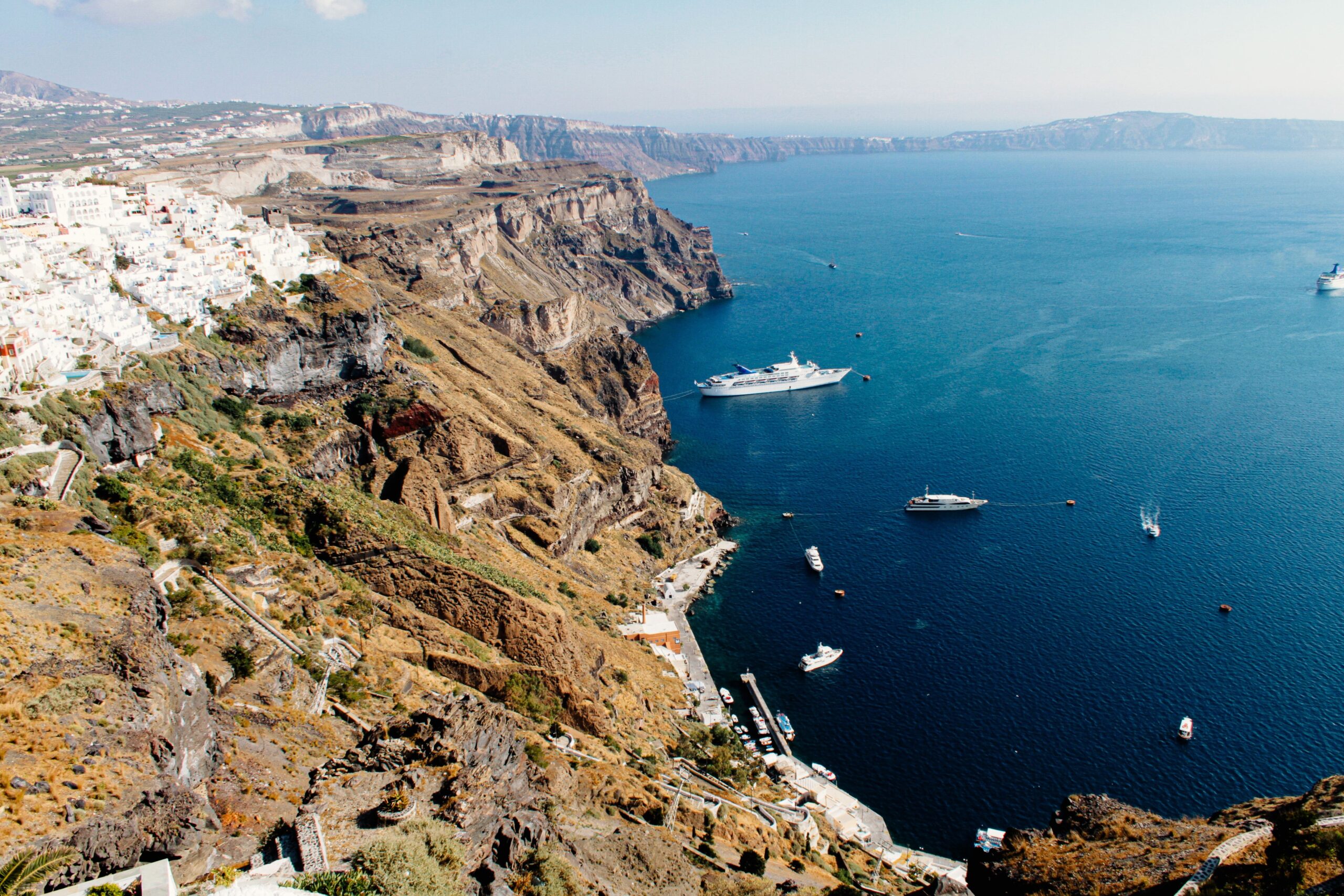 Wulkaniczne klify kaldery Santorini z białą zabudową Firy na szczycie i statkami na Morzu Egejskim, Grecja